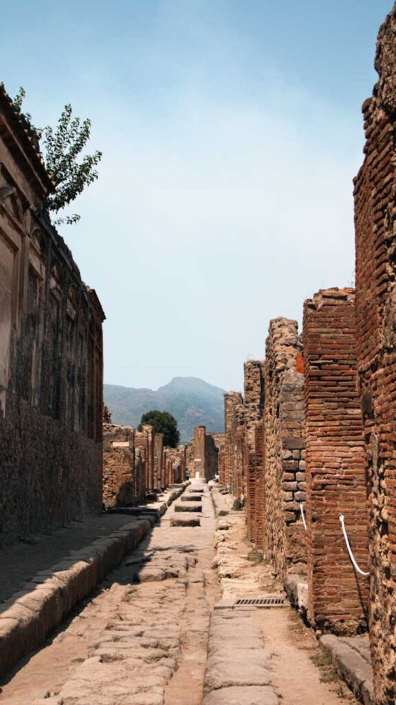 Stone-paved street lined with ruins in Pompeii with Mount Vesuvius in the background