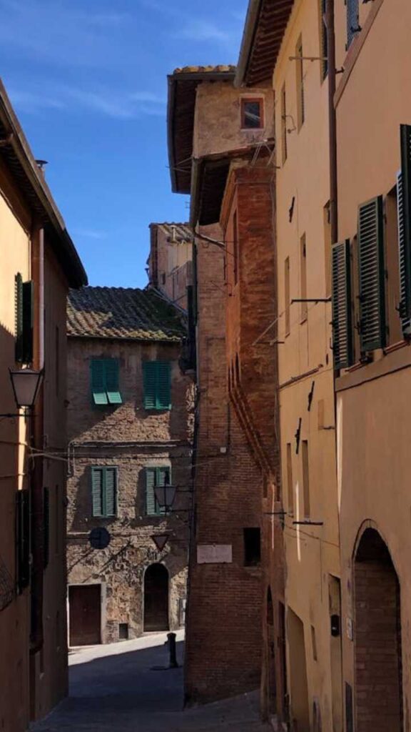 Quiet narrow street in Siena lined with rustic brick buildings and green shutters