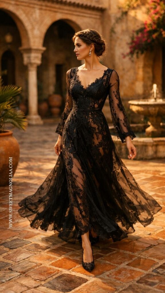 Bride in a long sleeve sheer black lace wedding dress with a flowing skirt, styled with heels in a warm-toned courtyard setting, showcasing elegant modern bridal style.