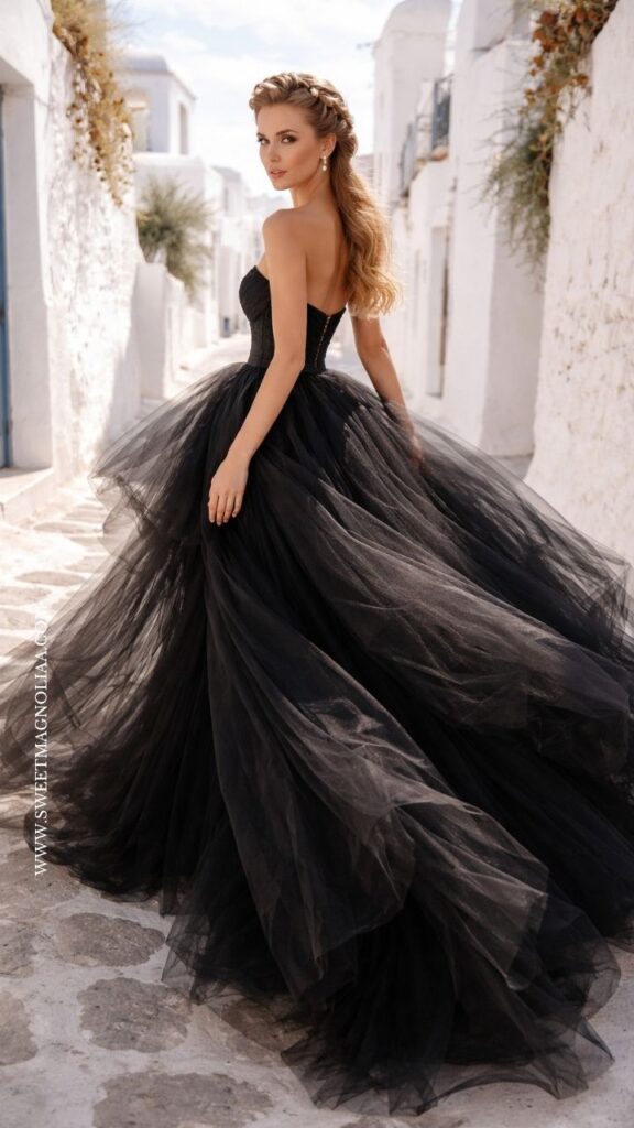Bride in a strapless black tulle ball gown wedding dress with a voluminous skirt and fitted bodice, walking through a bright white alley in a dramatic bridal look.