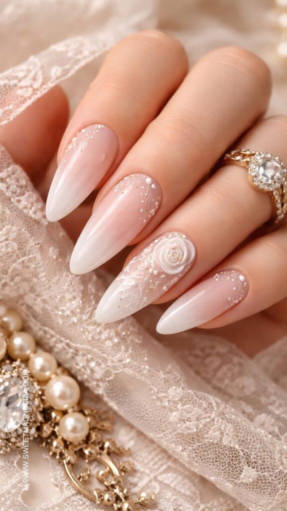 Blush pink ombre almond nails with delicate lace patterns, a white 3D rose accent, and tiny pearl and glitter details creating an elegant bridal manicure.