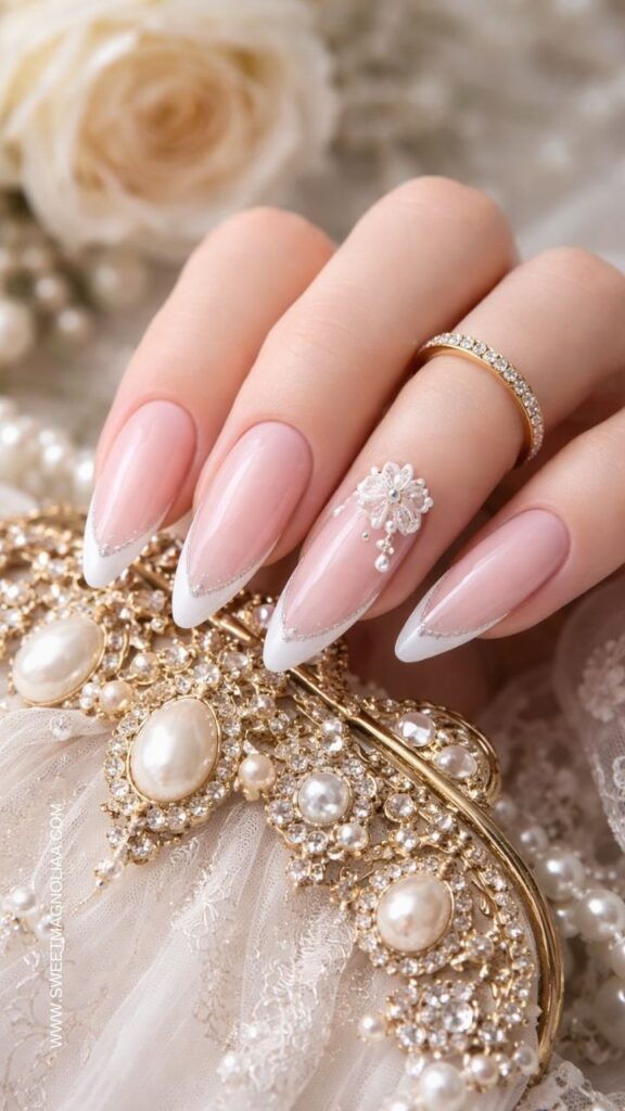 Blush pink almond nails with white French tips, delicate lace flower nail art, and a pearl drop accent creating a romantic bridal inspired manicure.