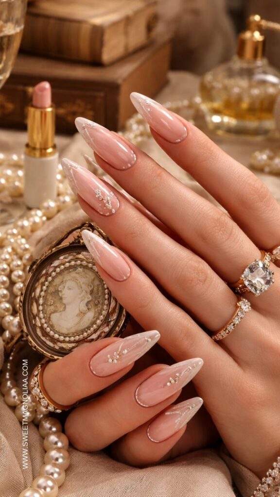 Blush pink almond nails with delicate white swirl lines and small crystal accents creating an elegant glossy manicure with subtle sparkle and bridal style.