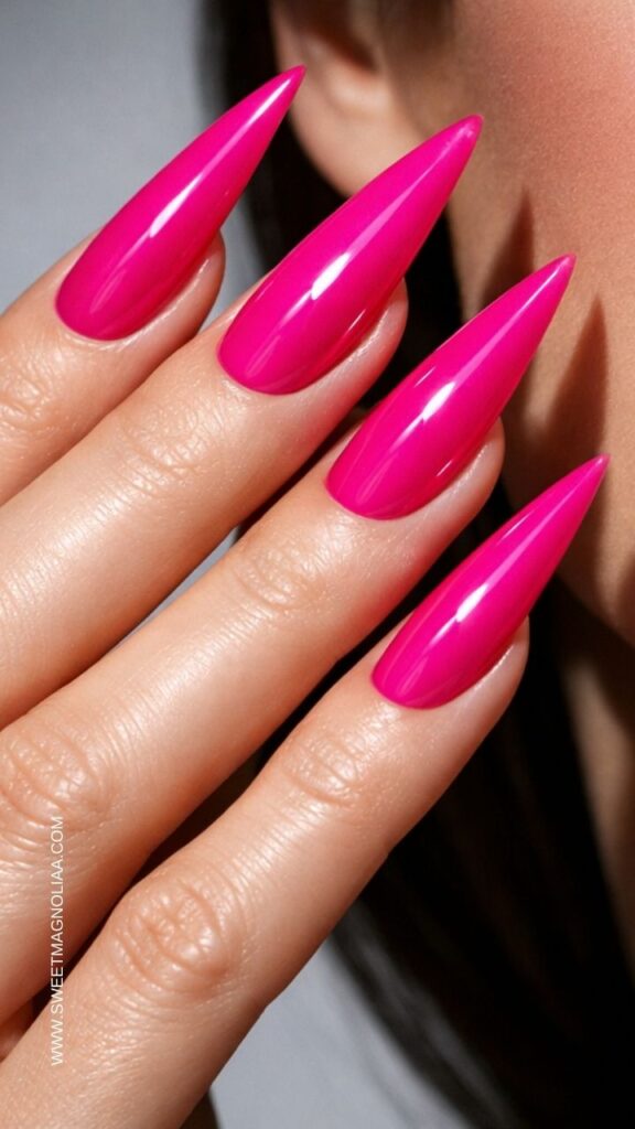 Glossy hot pink stiletto nails with a sleek, vibrant finish, creating a bold and modern manicure that highlights the dramatic pointed nail shape.