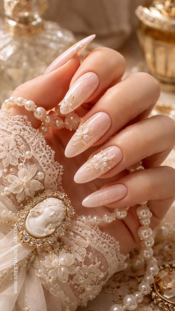 Blush pink almond nails with pearl flower accents, soft shimmer finish, and delicate gold details creating a romantic bridal inspired manicure.
