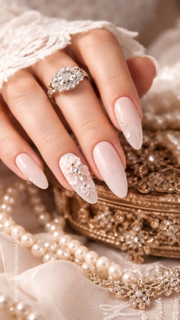 Blush pink ombre almond nails with a 3D floral accent, tiny pearls, and crystal details creating a romantic bridal manicure with soft shimmer.