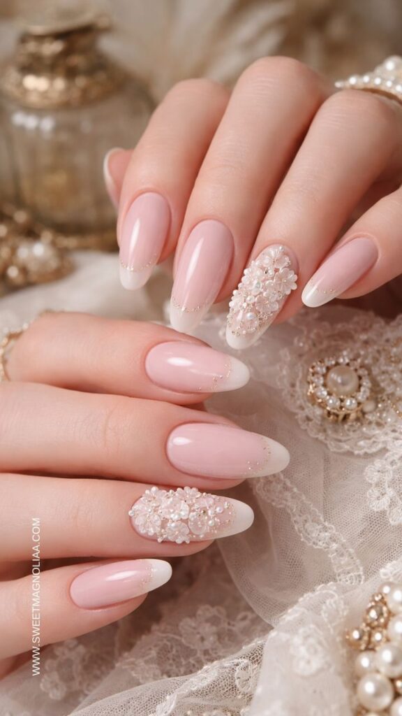 Blush pink almond nails with soft white French tips, gold shimmer outline, and a pearl floral cluster accent creating a romantic bridal inspired manicure.
