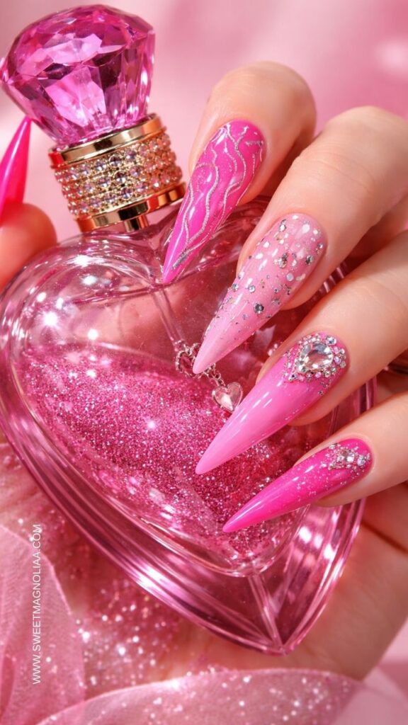Hot pink stiletto pink nail designs with rhinestones, glitter accents, and metallic swirl details styled over a sparkling pink perfume bottle, glamorous manicure idea.