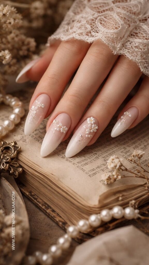 Blush pink ombre almond nails with pearl daisy flower accents and soft gold shimmer details creating an elegant romantic bridal manicure.
