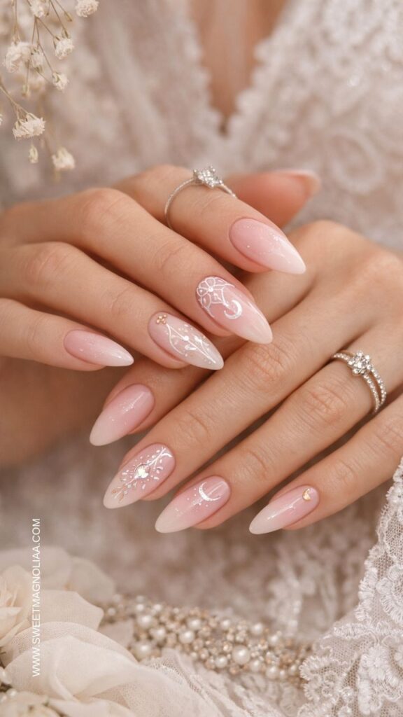 Soft blush pink almond nails with delicate white lace designs, tiny gold accents, and subtle shimmer, creating a romantic bridal manicure with an elegant finish.