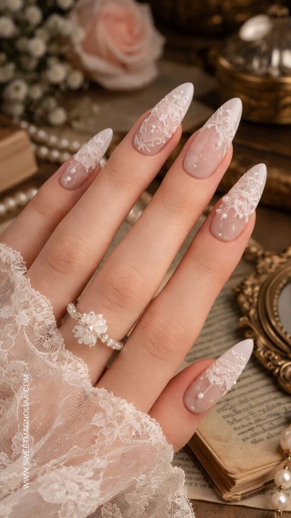 Blush pink almond nails with white French tips, intricate lace patterns, and pearl accents creating an elegant bridal inspired manicure.