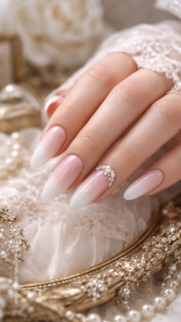 Blush pink ombre almond nails with milky white tips and a delicate crescent pearl accent creating an elegant minimalist bridal manicure.