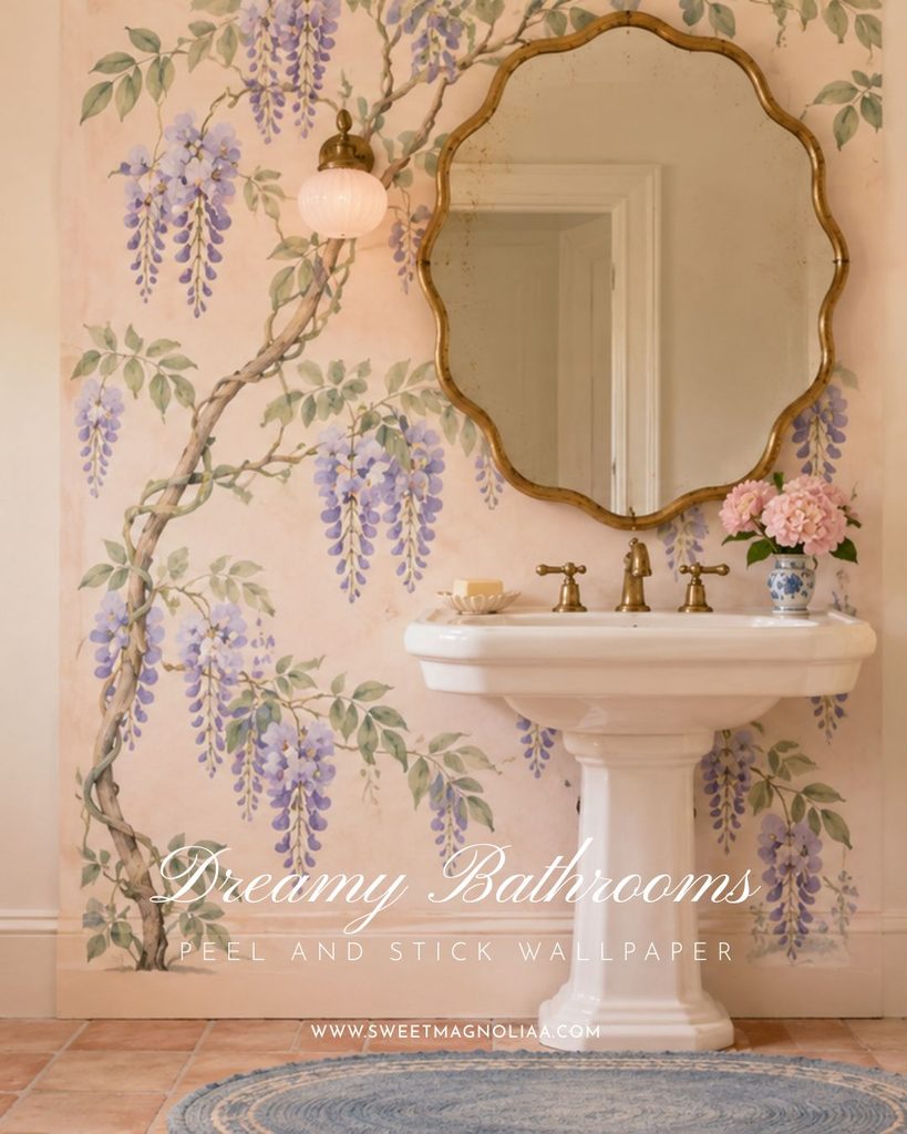Pedestal sink with brass taps beneath a scalloped gilt mirror on a blush wall with a wisteria mural, terracotta floor and blue rug in a cottage bathroom