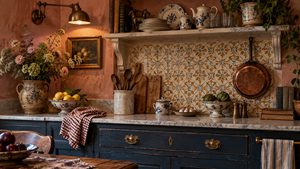 French cottage kitchen with deep blue cabinetry, patterned tile backsplash, marble countertops, copper cookware, blue-and-white pottery, vintage still-life art and warm terracotta plaster walls.
